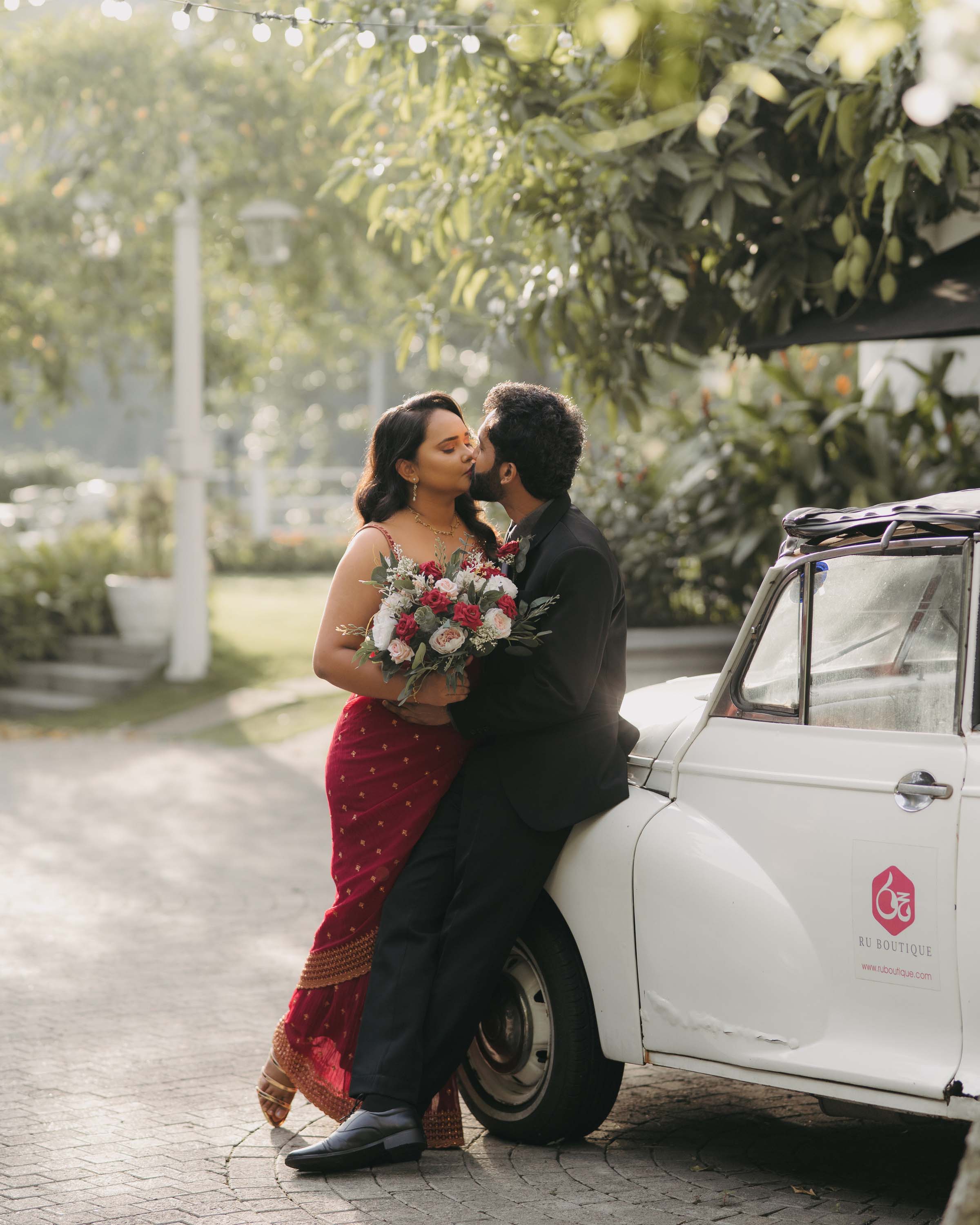 Romantic outdoor pre-wedding shoot with a classic white car and lush greenery.